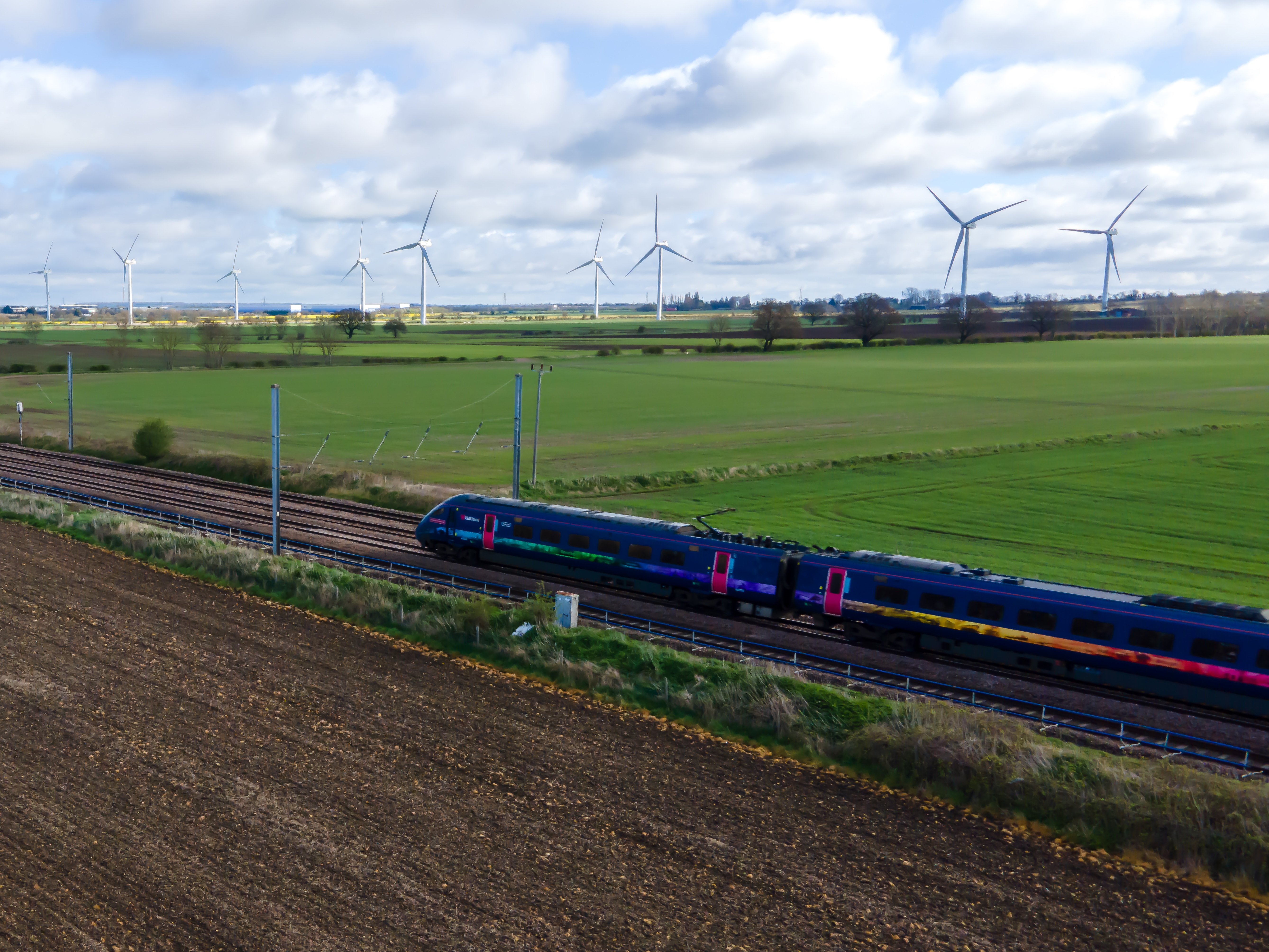 Train travelling past grass field and wind turbines